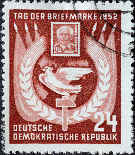 GERMANY, DDR - CIRCA 1952 : a postage stamp from Germany, GDR showing the 24 Pf-Pieck postage stamp, dove of peace, hammer and wreath of ears in front of flags. Day of the Postal stamp photo