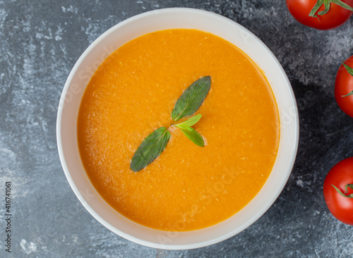 Delicious colored tomato cream-soup with herbs on grey background