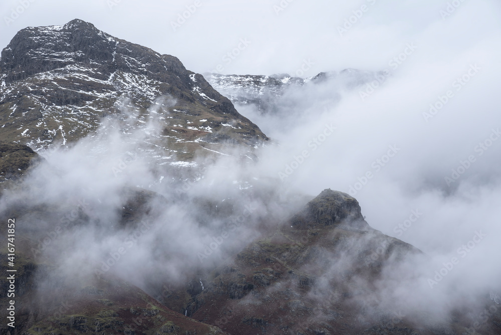 Epic Winter landscape image of view from Side Pike towards Langdale pikes with low level clouds on mountain tops and moody mist swirling around Epic Winter landscape image of view from Side Pike towards Langdale pikes with low level clouds on mountain tops and moody mist swirling around