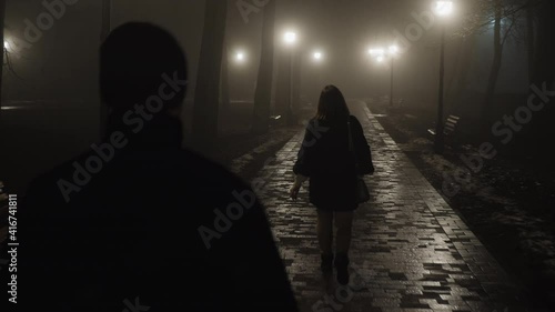 The man pursues the woman at night in a city park. Dangerous time on the street in the criminal world
