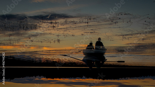 Two people are sailing in a boat. Beautiful sunset landscape over a Finnish lake. The space is flooded with gold. The picture is upside down.