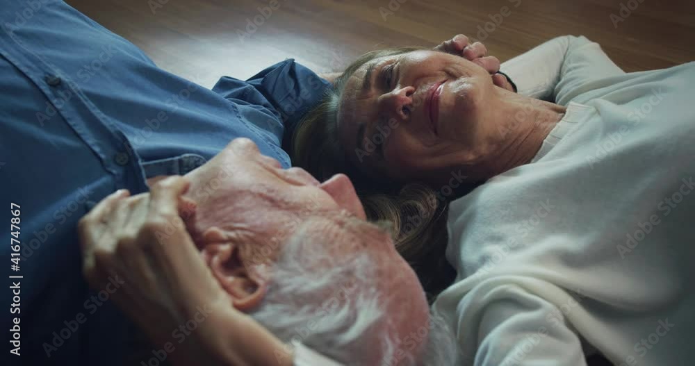 Cinematic shot of lovely happy mature couple is enjoying time together is speaking and caressing each other with affection while lying on floor at home. Concept: love, family, marriage, happiness, age Cinematic shot of lovely happy mature couple is enjoying time together is speaking and caressing each other with affection while lying on floor at home. Concept: love, family, marriage, happiness, age