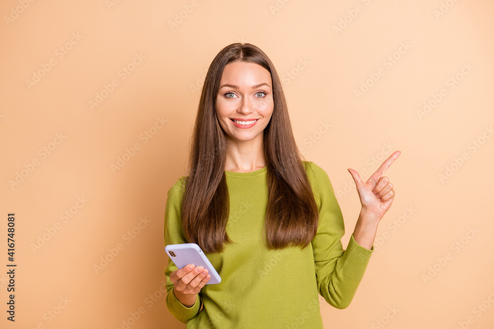 Photo of funny girl hold phone direct finger empty space wear green pullover isolated beige color background Photo of funny girl hold phone direct finger empty space wear green pullover isolated beige color background