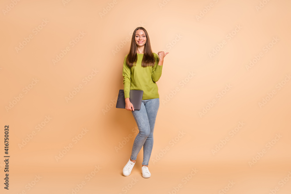 Photo of lady hold netbook indicate finger empty space wear green pullover jeans footwear isolated beige color background Photo of lady hold netbook indicate finger empty space wear green pullover jeans footwear isolated beige color background