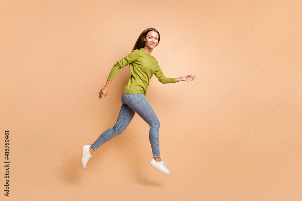 Profile photo of energetic girl jump go wear green sweater jeans sneakers isolated beige color background