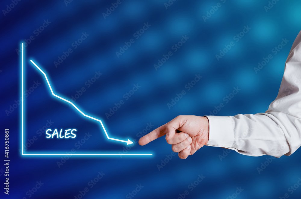 Businessman hand points to the word sales with a decreasing chart or graph.