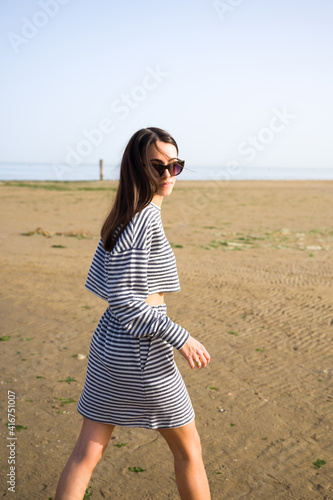 beautiful girl in striped dress and sunglasses walks on the beachon the beach