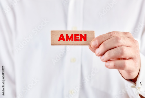фотографія Male hand showing a wooden block with the word Amen.