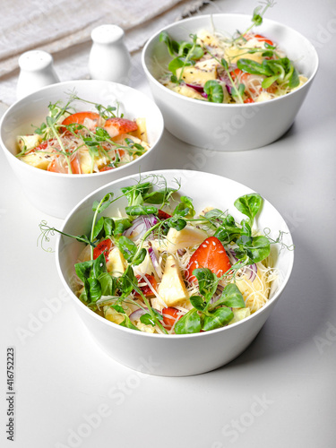 Fruit salad with strawberries, pineapple pieces, herbs, red onions and cheese in white ceramic bowls on a light background. Ideas and recipes for a healthy diet. Vegeterian food. Vertical shot