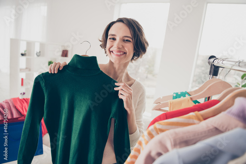 Photo of positive nice young woman smile hold sweater show room choose buy shopper indoors inside house