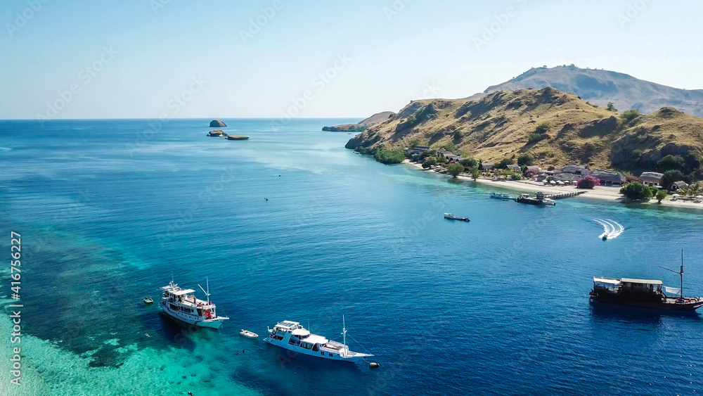A top down drone shot of paradise island in Komodo National Park, Flores, Indonesia. The island has scarcely any trees and bushes and is surrounded with idyllic white sand beaches. Island hoping