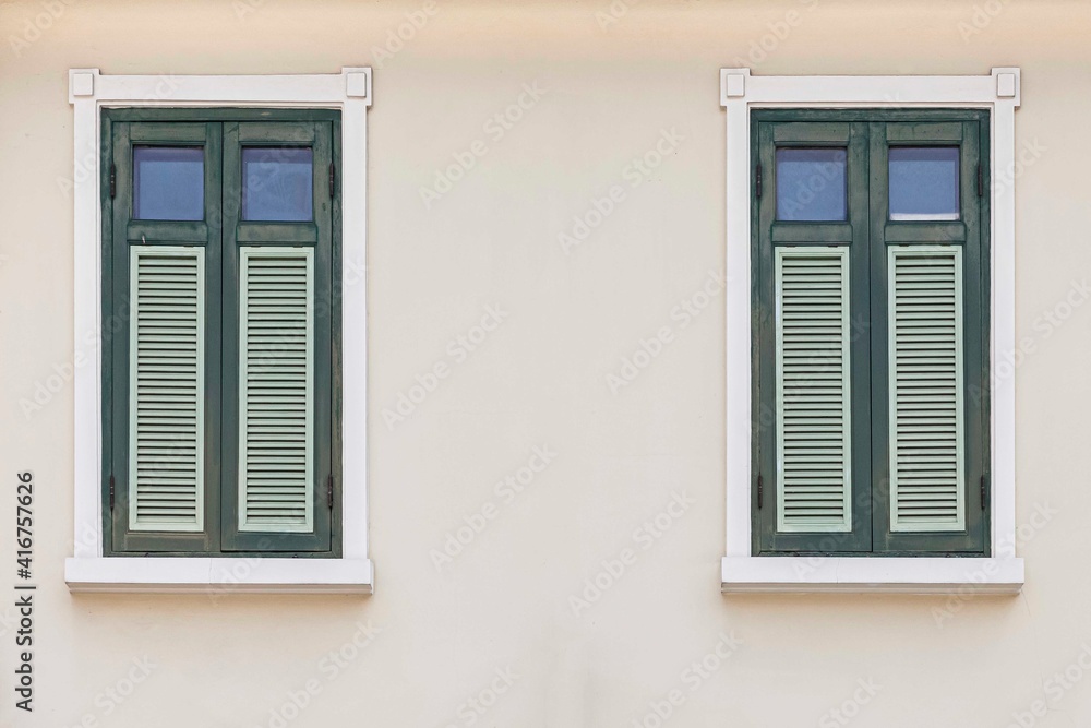 Two vintage green shuttered wooden windows and cream colored facades