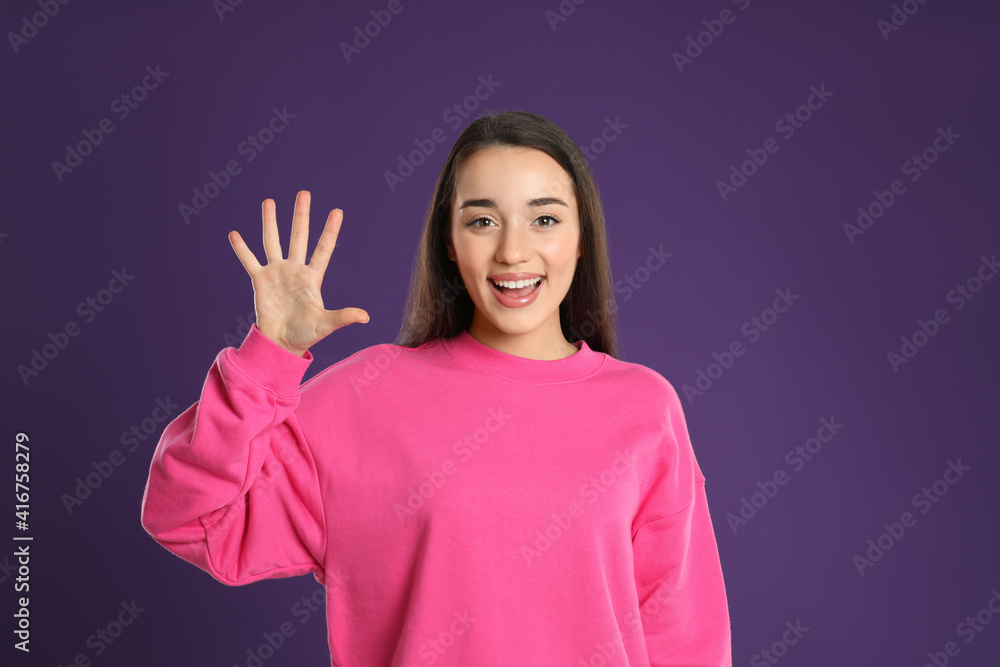 Woman showing number five with her hand on purple background Woman showing number five with her hand on purple background