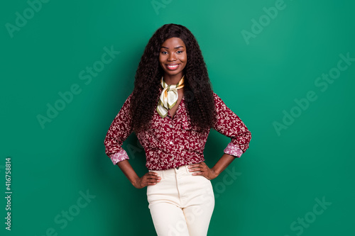 Photo of sweet charming wavy dark skin lady wear print shirt smiling arms waist isolated green color background © deagreez