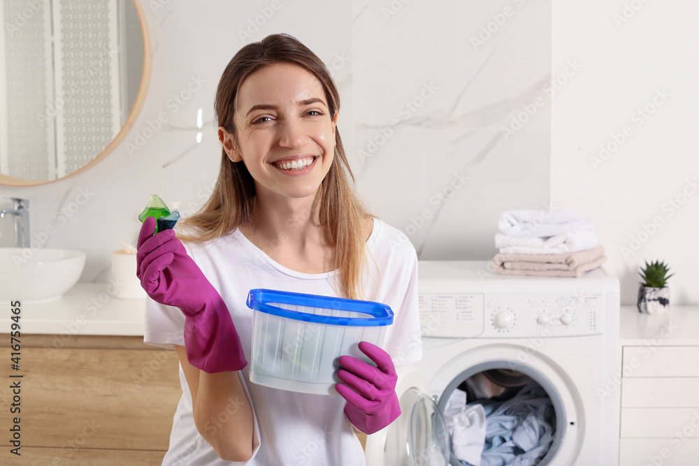 Woman holding container with laundry detergent capsules in bathroom Woman holding container with laundry detergent capsules in bathroom