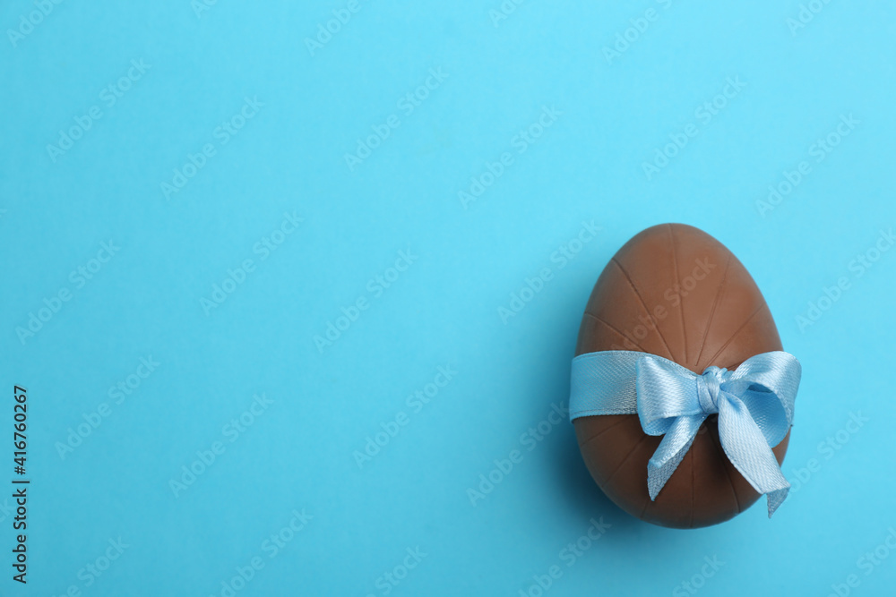 Fototapeta premium Sweet chocolate egg with bow on light blue background, top view. Space for text
