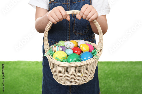 Little girl with basket full of Easter eggs on green grass against white background, closeup