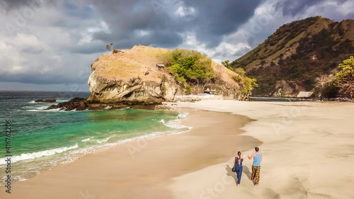 A couple walking on an idyllic Koka Beach. Hidden gem of Flores, Indonesia. Couple is enjoying their romantic escape. Waves gently washing the shore. There are hills in the back. Happiness and love © Chris