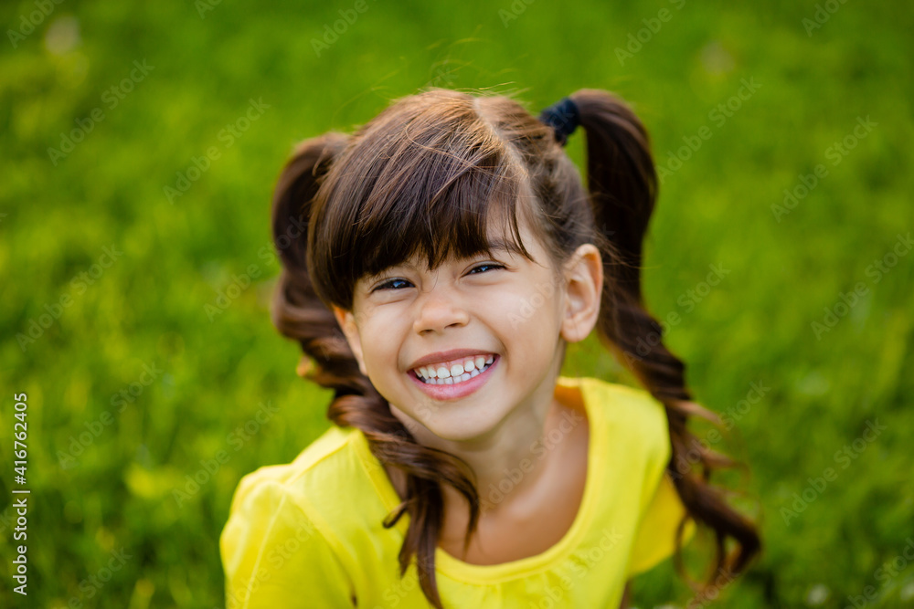 Happy little Indian girl in yellow T-shirt laughs summer on the lawn Happy little Indian girl in yellow T-shirt laughs summer on the lawn