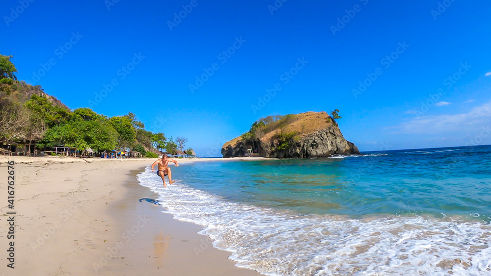 Fototapeta premium A man jumping into the waves on idyllic Koka Beach. Hidden gem of Flores, Indonesia. He is having a lot of fun, collecting happy moments. Adventure and discovering while travelling