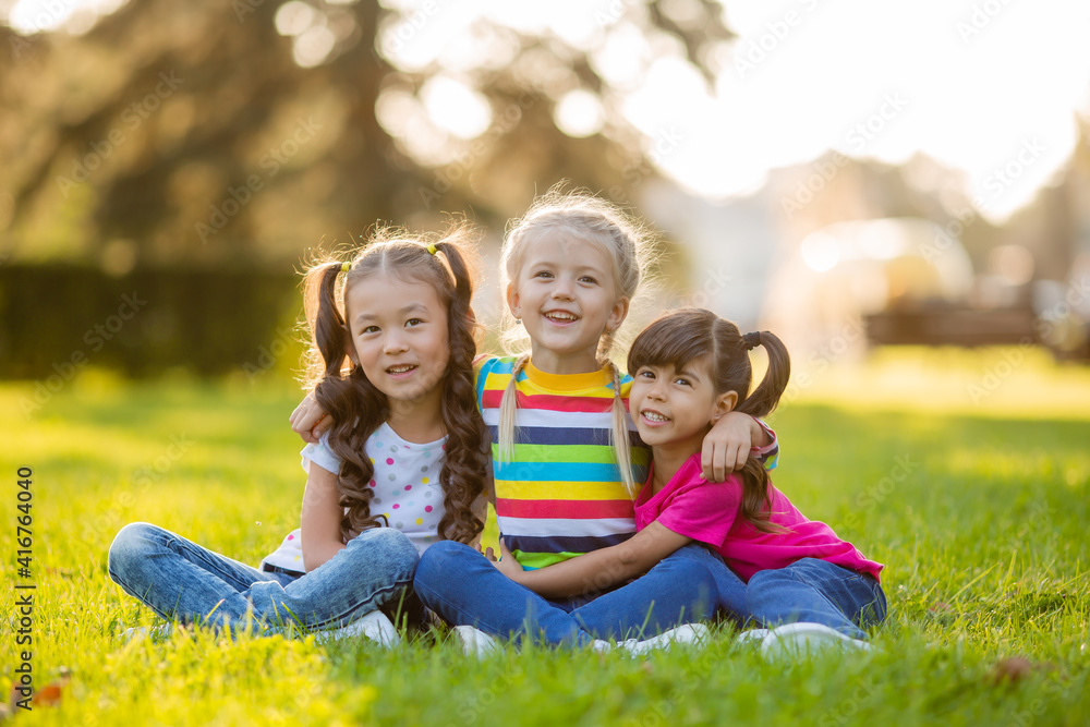 three little girls cuddle in the summer on the lawn. International Children's Day