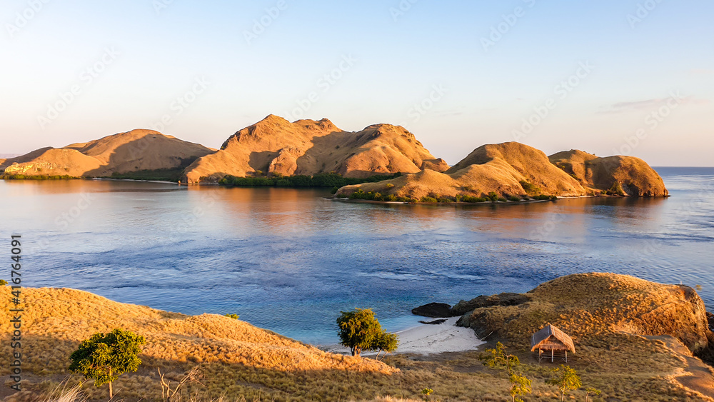 A view on a the morning sun rising over an island formation in Komodo National Park, Flores, Indonesia. Golden hour over the islands and sea. Idyllic landscape. New day beginning. Chocolate hills.