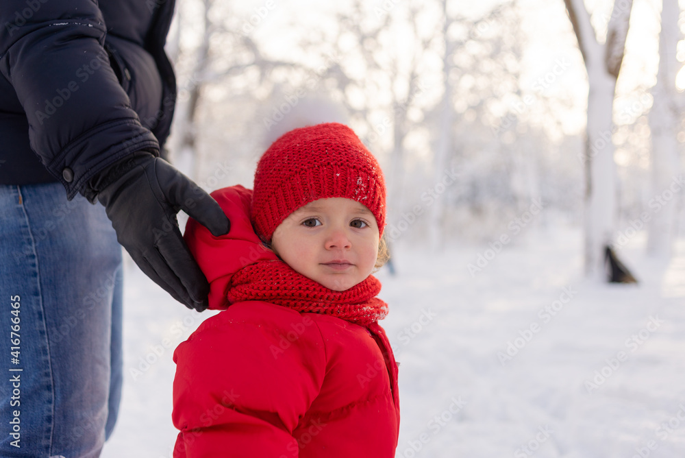 Portrait of a little girl in a knitted hat and red overalls, she is standing in a snowy park, and her dad is holding her. Portrait of a little girl in a knitted hat and red overalls, she is standing in a snowy park, and her dad is holding her.