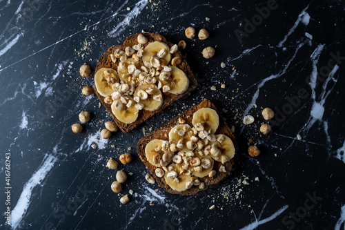 Peanut butter banana toast with roasted hazlenuts on black marble background.