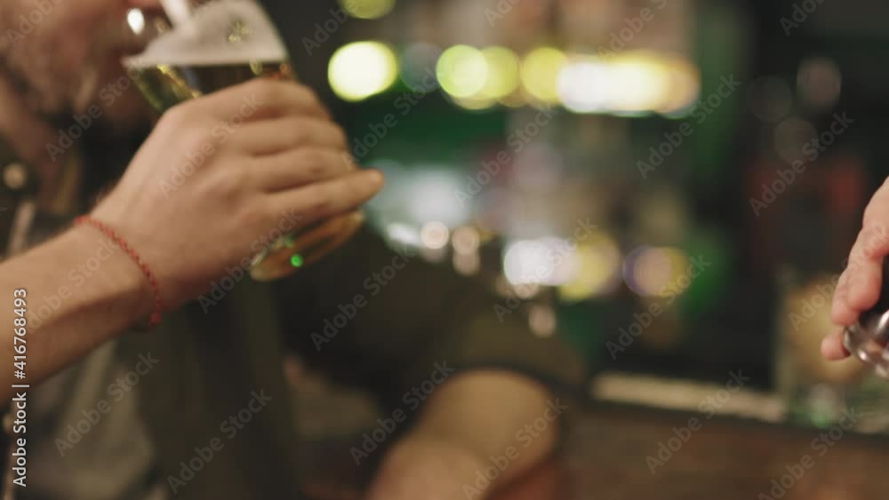 Slow-motion close-up of unrecognizable male friends toasting beer glasses at bar