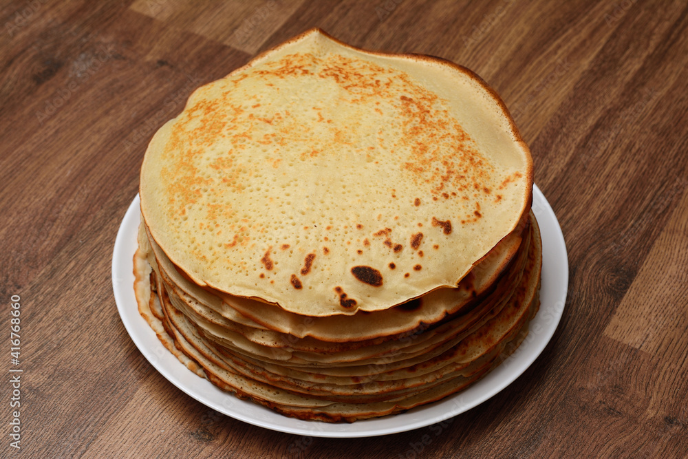 Pancakes on a white plate on a table with a wooden texture, close-up