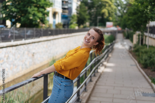 Fun vivacious young woman leaning on a river railing