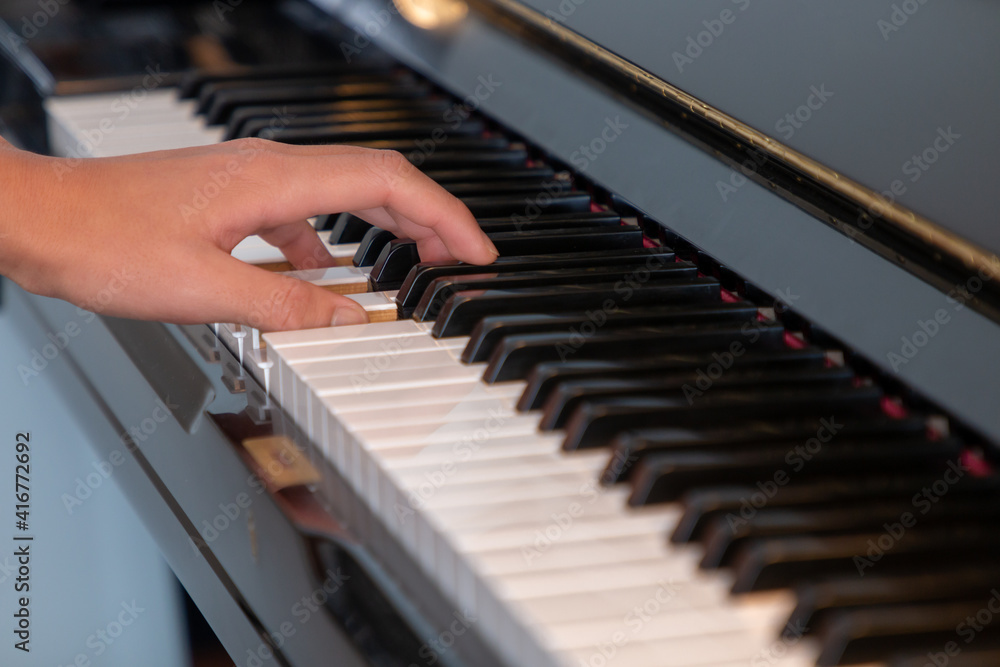 Black glossy upright piano with white ivory keys being played with one hand closeup