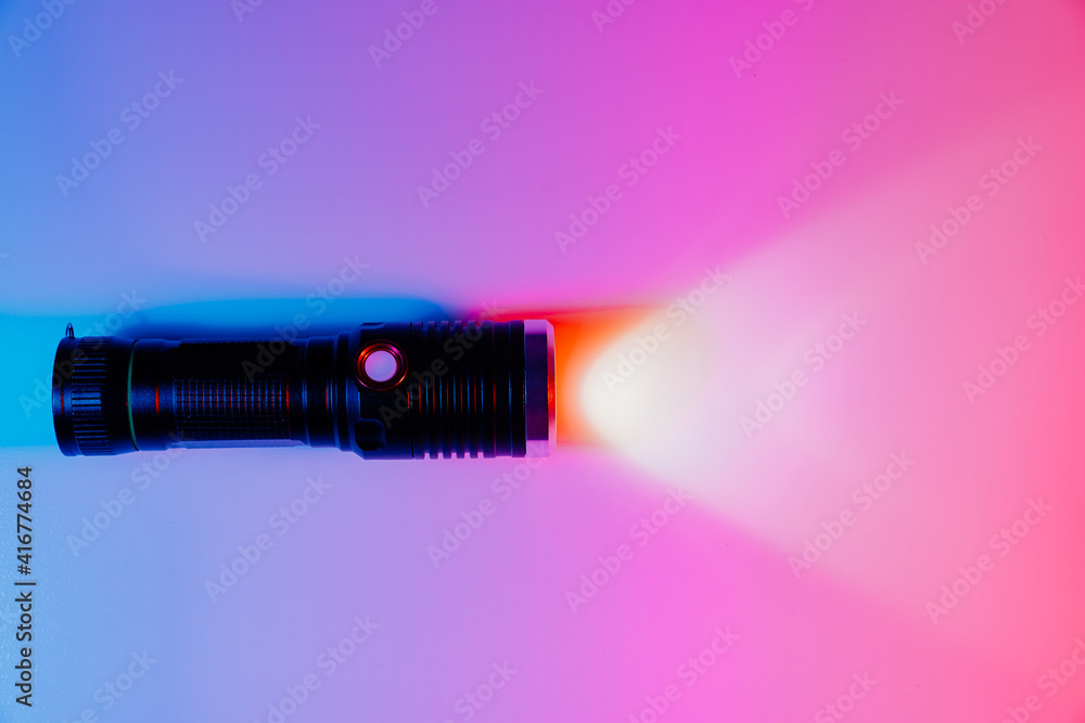 A small black flashlight in colored lighting. A small black flashlight in colored lighting.