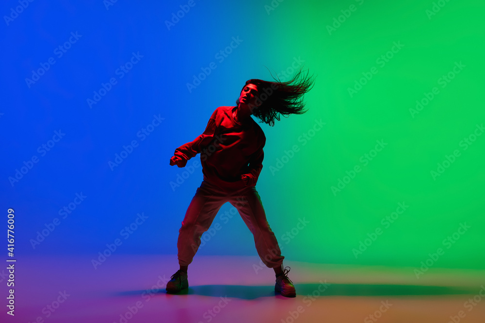 Night. Stylish sportive girl dancing hip-hop in stylish clothes on colorful background at dance hall in neon light. Youth culture, movement, style and fashion, action. Fashionable bright portrait.