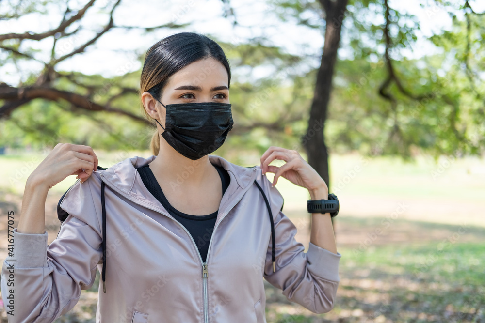 Selective focus at face of young beautiful Asian women wearing surgical face mask to prevent Covid-19 while warm up before exercise or running at the park in the morning. New normal lifestyle concept. Selective focus at face of young beautiful Asian women wearing surgical face mask to prevent Covid-19 while warm up before exercise or running at the park in the morning. New normal lifestyle concept.