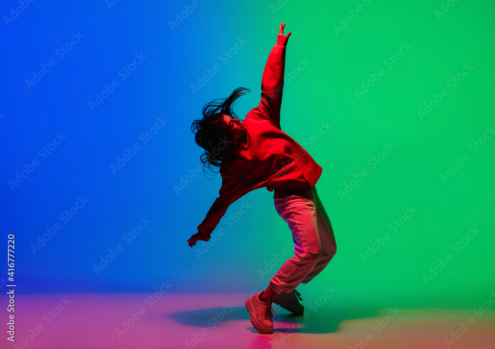 Inspiration. Stylish sportive girl dancing hip-hop in stylish clothes on colorful background at dance hall in neon light. Youth culture, movement, style and fashion, action. Fashionable bright - obrazy, fototapety, plakaty 