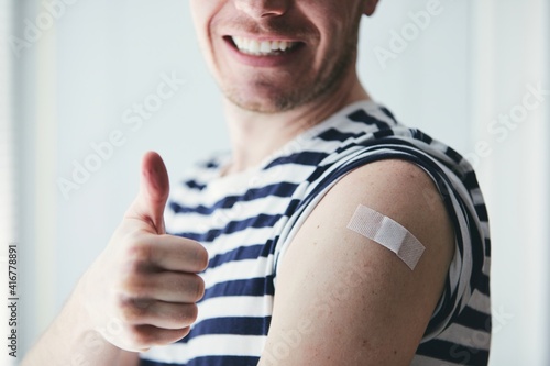 Happy young man showing thumb up and his arm after vaccination. Themes prevention, vaccine and health care during pandemic covid-19. photo