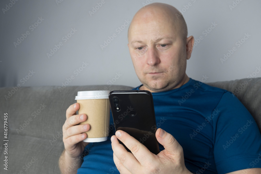 man uses a smartphone and drinks coffee sitting on the couch man uses a smartphone and drinks coffee sitting on the couch