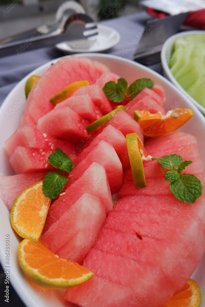 Fresh red watermelon slices on a plate with the addition of fresh orange and mint leaves Fresh red watermelon slices on a plate with the addition of fresh orange and mint leaves