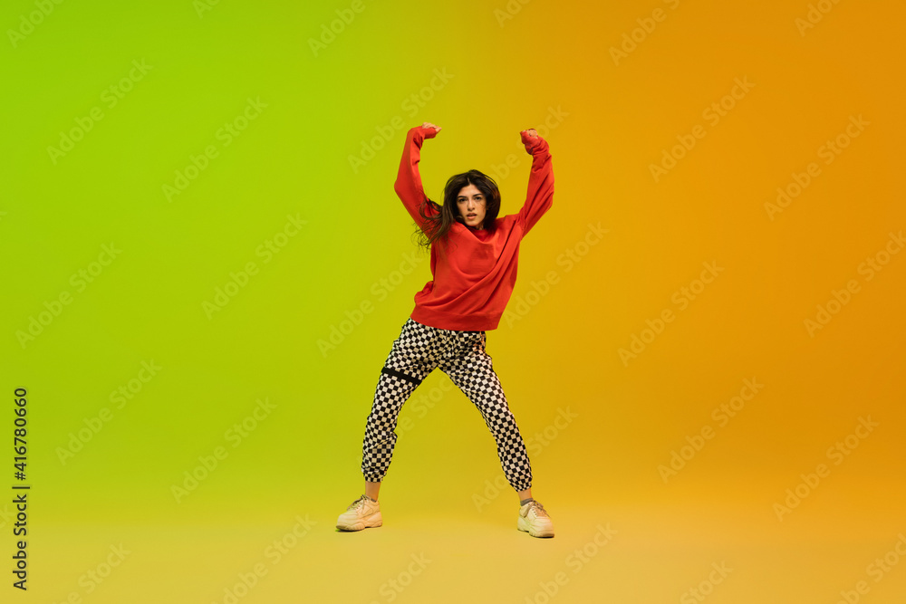 Dynamic. Stylish sportive girl dancing hip-hop in stylish clothes on colorful background at dance hall in neon light. Youth culture, movement, style and fashion, action. Fashionable bright portrait.