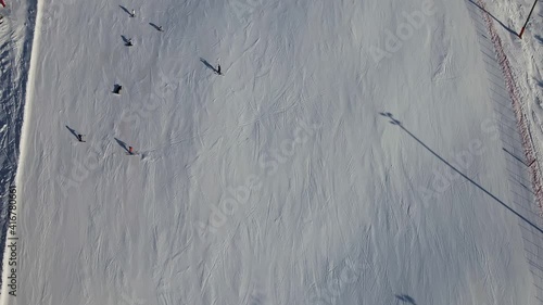 People skiing down a steep slope at a ski holiday resort in the mountains. Top down aerial view.