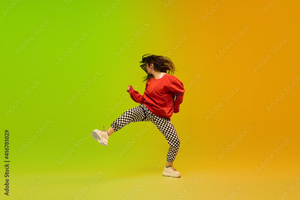 Action. Stylish sportive girl dancing hip-hop in stylish clothes on colorful background at dance hall in neon light. Youth culture, movement, style and fashion, action. Fashionable bright portrait.