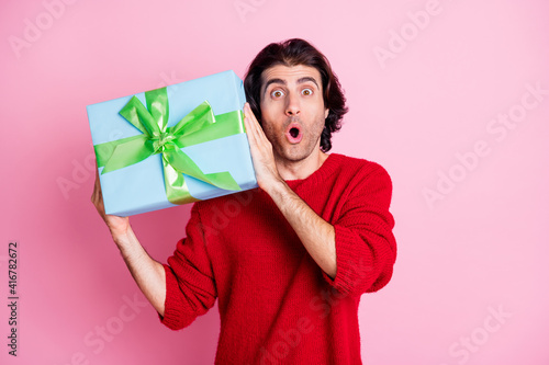 Photo portrait of shocked man shaking present near ear guessing what's inside isolated on pastel pink colored background © deagreez
