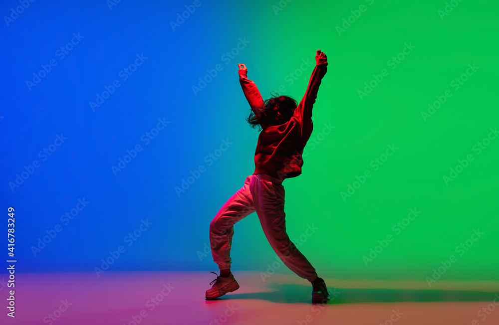 Modern. Stylish sportive girl dancing hip-hop in stylish clothes on colorful background at dance hall in neon light. Youth culture, movement, style and fashion, action. Fashionable bright portrait.