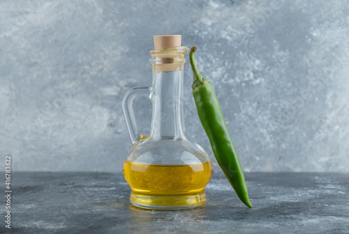 Close up photo of green hot pepper with bottle of oil on grey background