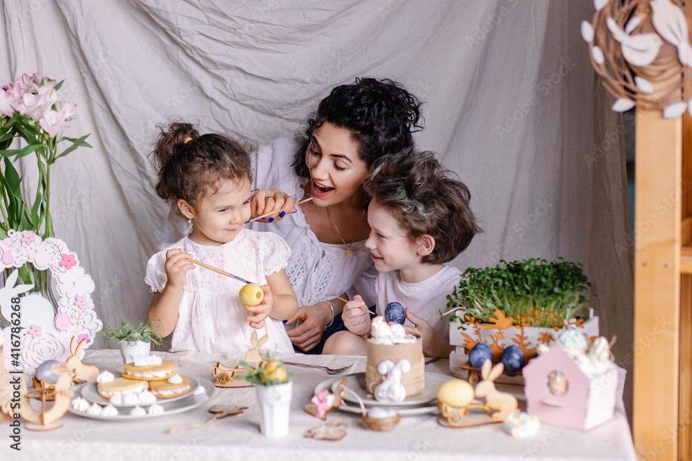 Happy family is preparing for Easter. Mother and children paint eggs together for fun. joy life moments lifestyle. Festive dinner on a decorated table. Mix race kids. Christian traditions of spring Happy family is preparing for Easter. Mother and children paint eggs together for fun. joy life moments lifestyle. Festive dinner on a decorated table. Mix race kids. Christian traditions of spring