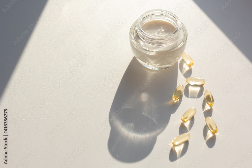 Skin care and supplements for clear and radiant skin. Closeup of a jar of moisturizer and vitamin A and E capsules.