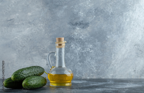 Stack of fresh cucumber and bottle of oil over grey background