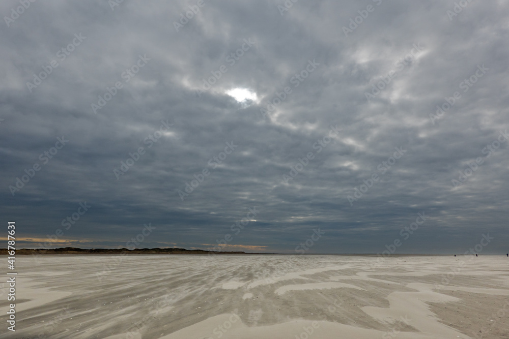 Storm blowing sand over the vast beach under a dark sky in winter