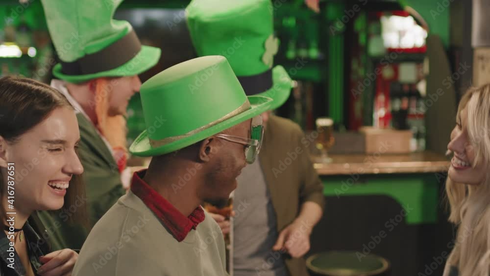 Slow-motion medium closeup of joyful multi-ethnic friends in funny Irish costumes partying together in local pub dancing and laughing Slow-motion medium closeup of joyful multi-ethnic friends in funny Irish costumes partying together in local pub dancing and laughing